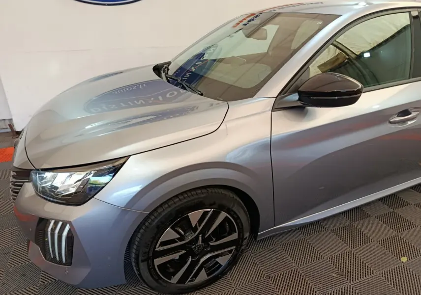 Vue 3/4 avant gauche d'une Peugeot 208 gris clair avec jantes alliage noires et rétroviseur noir brillant.