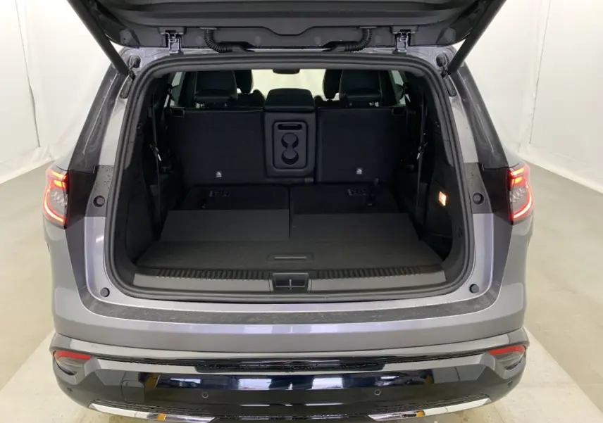 Coffre ouvert vu de l'arrière d'un Renault Espace gris schiste avec banquette arrière rabattue et feux arrière allumés.