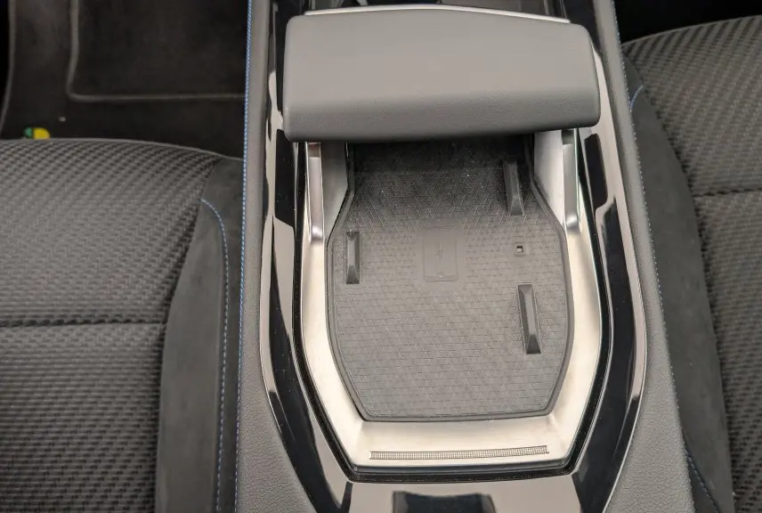 Gros plan sur le chargeur à induction central entouré de la sellerie mixte tissu carbone et alcantara avec surpiqûres bleues du Renault Espace gris Schiste.