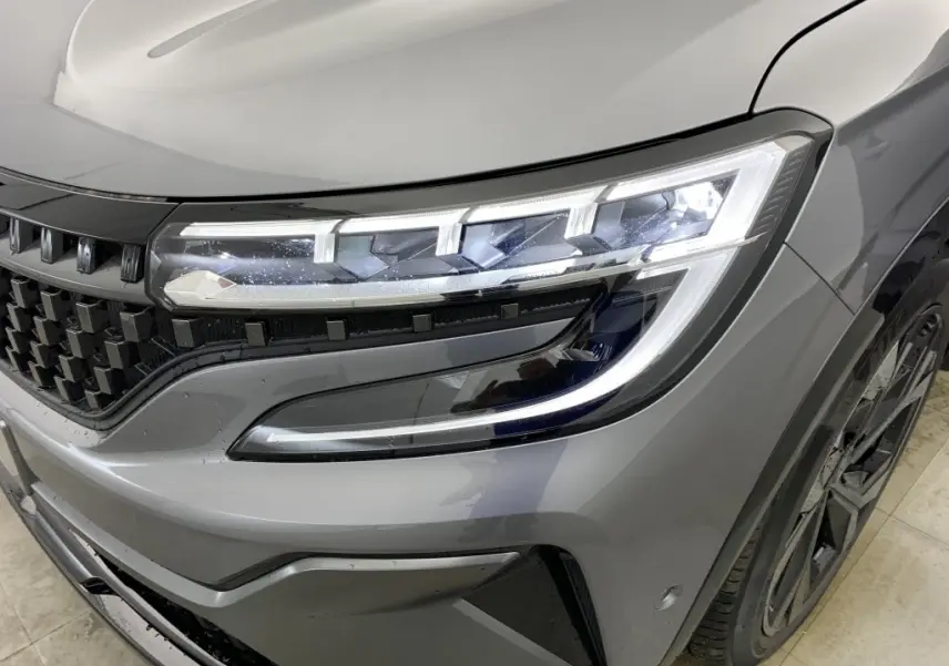 Gros plan sur le phare avant droit et la calandre à damiers du Renault Espace E-Tech gris schiste finition Esprit Alpine.