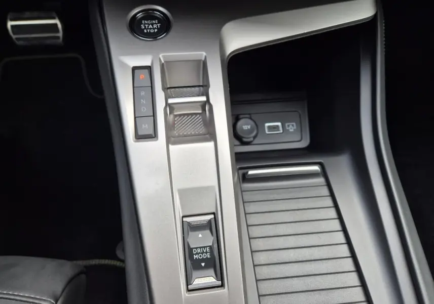 Vue rapprochée de la console centrale argentée du Peugeot 408 Hybrid 136 e-DCS6 GT avec levier de vitesse et bouton Drive Mode.