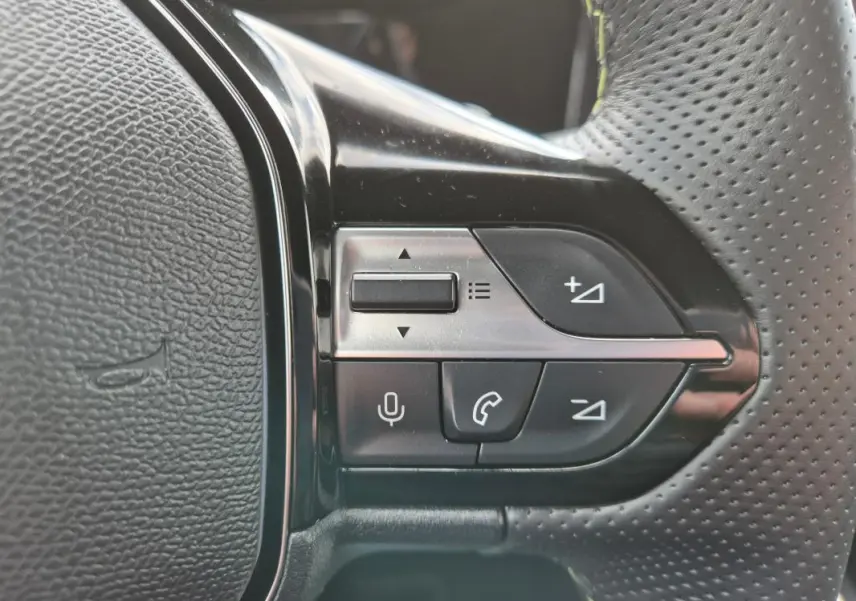 Gros plan sur les commandes gauche du volant cuir perforé du Peugeot 408 Hybrid 136 e-DCS6 GT noir 2024.