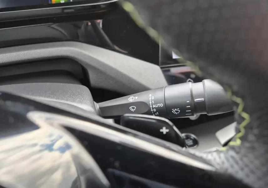 Gros plan sur la commande d’essuie-glace à gauche du volant cuir noir du Peugeot 408 Hybrid 2024.