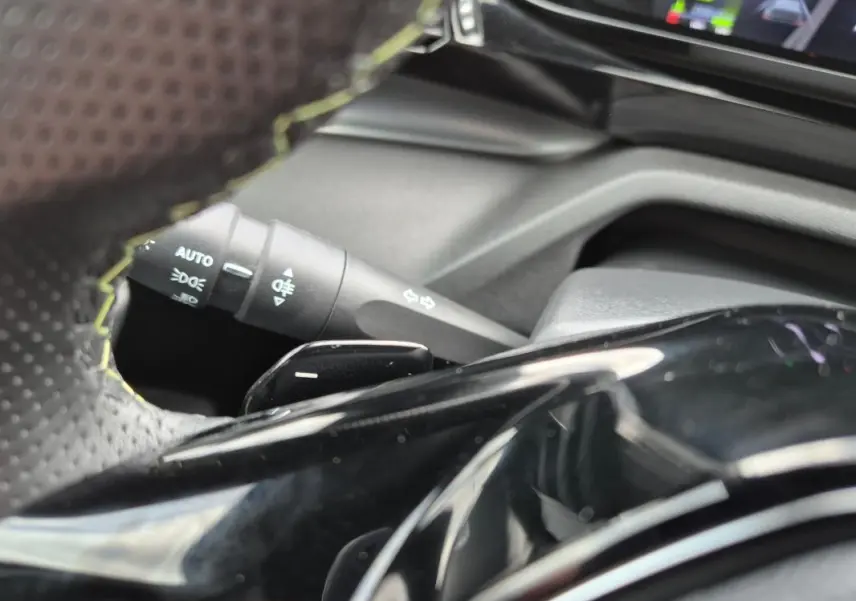 Gros plan sur le volant cuir et la commande des feux d’un Peugeot 408 Hybrid 136 e-DCS6 GT noir, intérieur moderne.