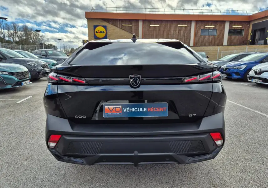 Vue arrière d'une Peugeot 408 noire 2024 avec feux LED distinctifs et logo lion central sur parking extérieur.