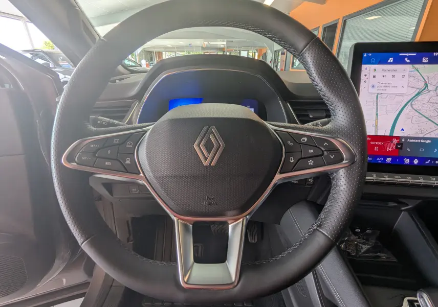 Vue intérieure centrée sur le volant en cuir perforé de la Renault Symbioz E-Tech, avec écran tactile et tableau de bord numérique.