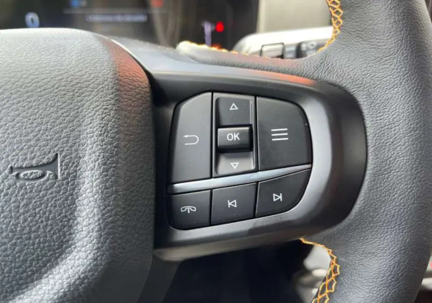 Gros plan sur les commandes multifonctions à droite du volant cuir noir avec surpiqûres orange du Ford Ranger Wildtrak 2025.