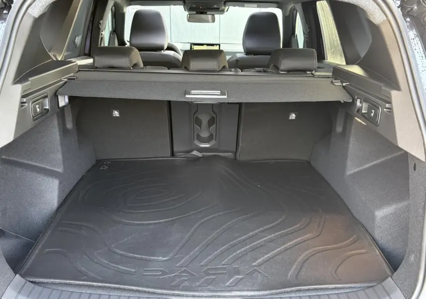 Vue depuis le hayon ouvert sur le coffre spacieux du Dacia Bigster 2026 avec tapis de sol noir et banquette arrière rabattable.