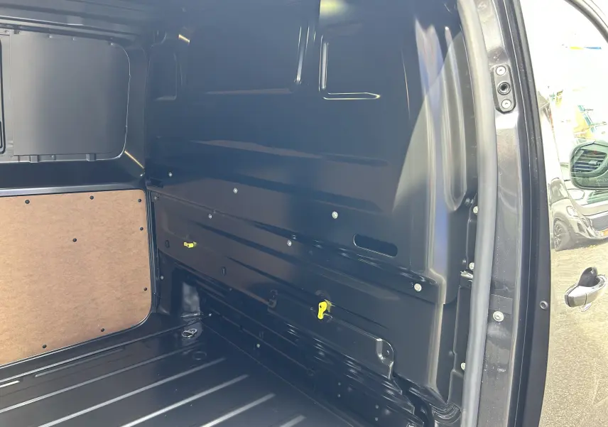 Vue intérieure côté droit du fourgon Citroën Jumpy gris acier, montrant la paroi métallique et un panneau en bois.