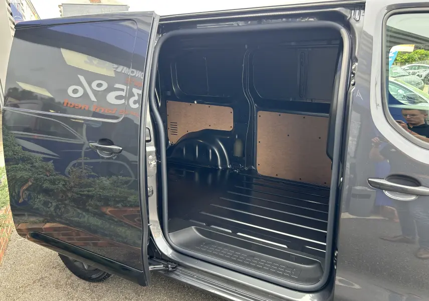 Vue latérale gauche du Citroën Jumpy Fourgon gris acier avec porte coulissante ouverte dévoilant l'espace de chargement vide.