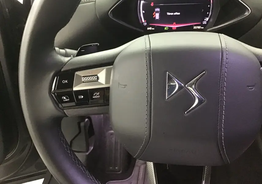 Gros plan sur le volant cuir noir du DS3 Crossback 2024 avec commandes intégrées et logo DS au centre.