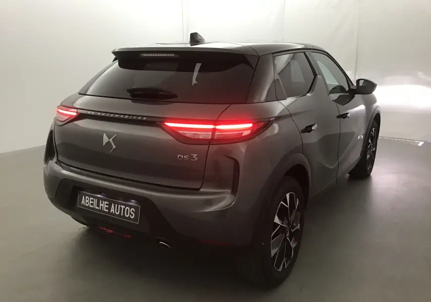 Vue 3/4 arrière droite d'un DS3 Crossback gris platinium 2024 avec feux arrière allumés dans un studio blanc.