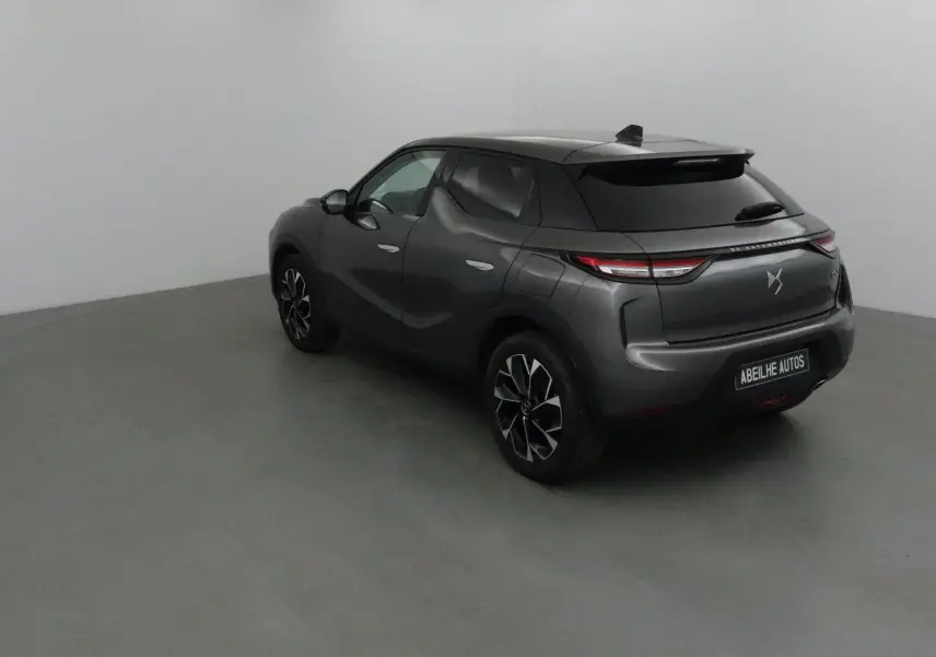 Vue 3/4 arrière droite d'un DS3 Crossback gris platinium avec jantes noires et feux arrière LED allumés.