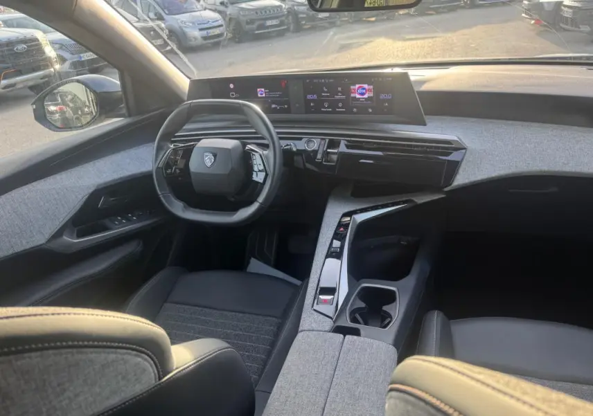 Vue intérieure avant du Peugeot 3008 Hybrid 145 Allure 2025, tableau de bord moderne avec cockpit numérique et sellerie grise.