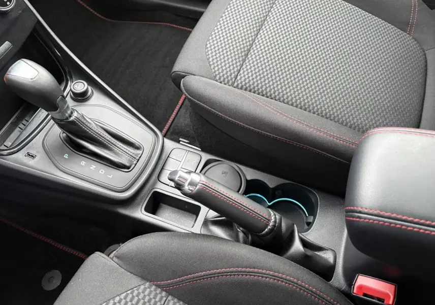 Vue rapprochée de la console centrale du Ford Puma 2024, sièges noirs avec surpiqûres rouges et levier de vitesse automatique.