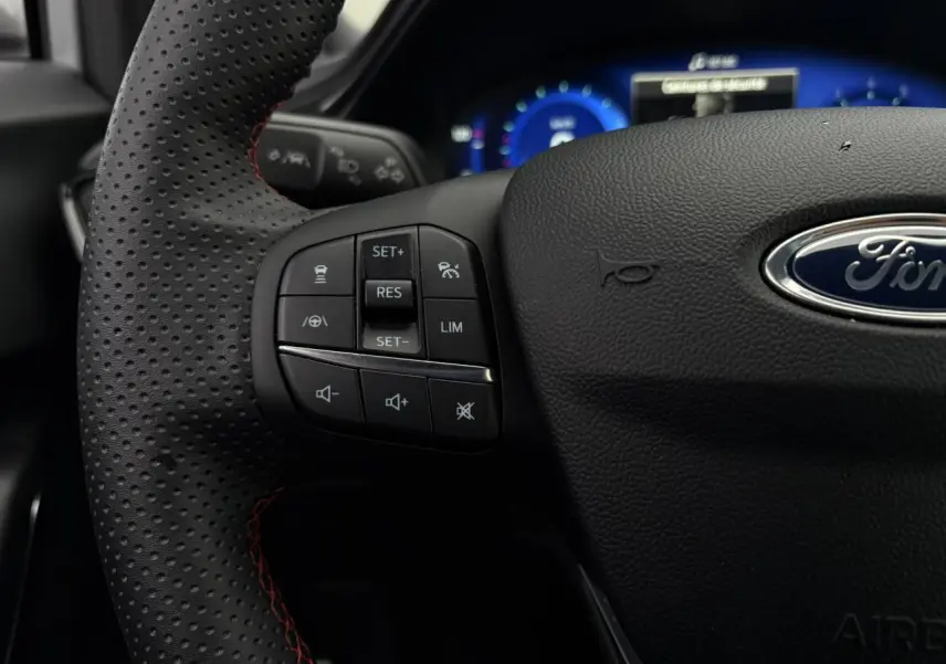 Gros plan sur le volant perforé noir avec surpiqûres rouges du Ford Puma 2024, boutons de commande multifonctions visibles.