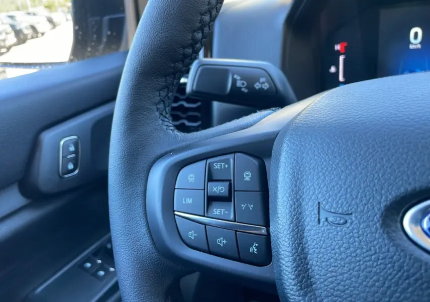 Gros plan sur le volant cuir noir du Ford Ranger 2025, avec commandes multifonctions et tableau de bord numérique en arrière-plan.