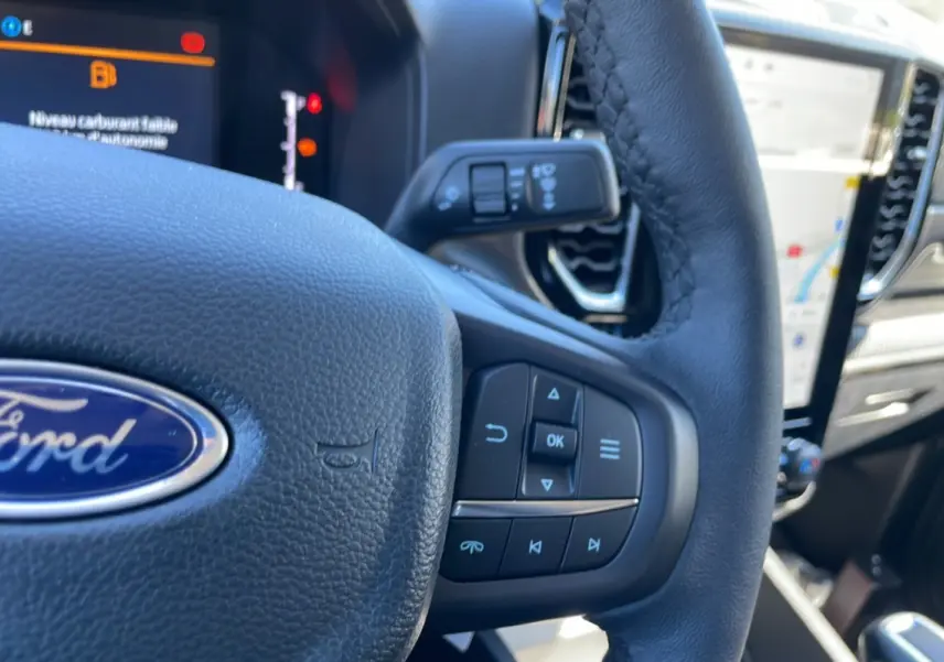 Gros plan sur le volant cuir multifonctions du Ford Ranger 2025, avec écran tactile et commandes au volant visibles.
