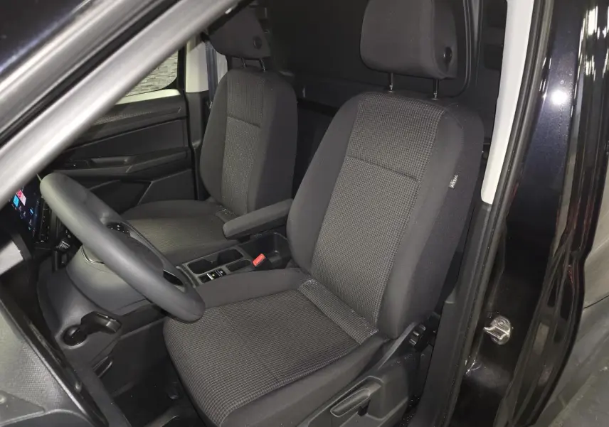Vue intérieure côté conducteur du Volkswagen Caddy Cargo noir 2024, sièges tissu noir avec accoudoir et tableau de bord visible.
