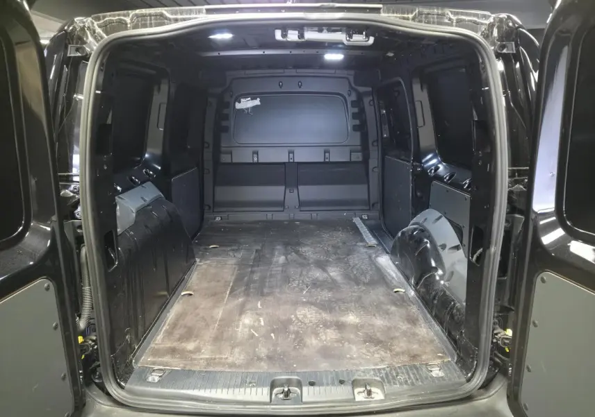 Vue arrière ouverte du coffre noir du Volkswagen Caddy Cargo 2024, montrant l'espace de chargement vide avec revêtement caoutchouc.