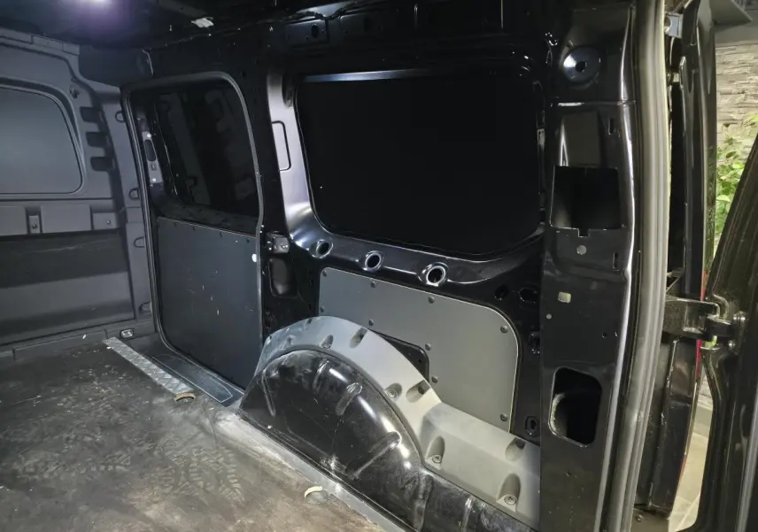 Vue intérieure arrière droite du Volkswagen Caddy Cargo noir 2024, montrant l'espace de chargement tôlé et le passage de roue.