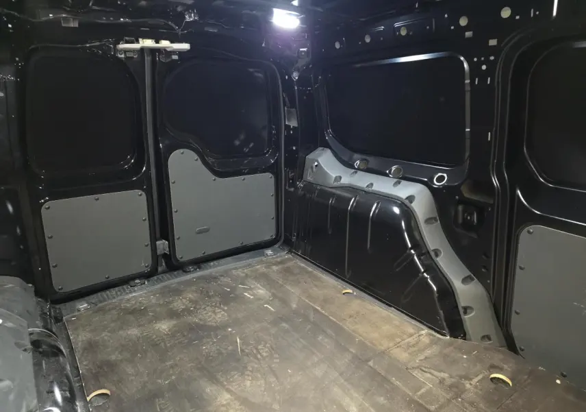 Vue intérieure arrière du Volkswagen Caddy Cargo noir 2024, montrant l'espace de chargement avec plancher en bois et parois renforcées.