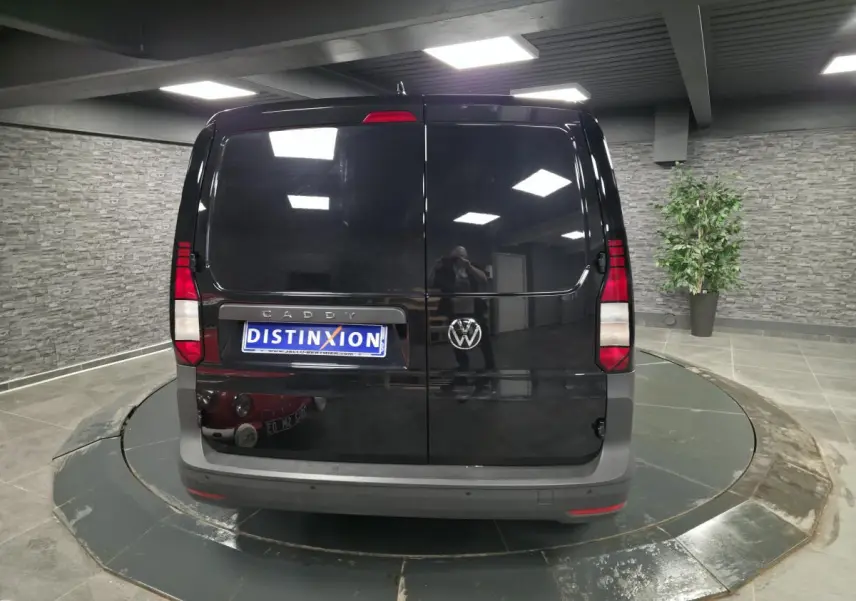 Vue arrière d'un Volkswagen Caddy Cargo noir avec portes battantes et pare-chocs gris dans un showroom.