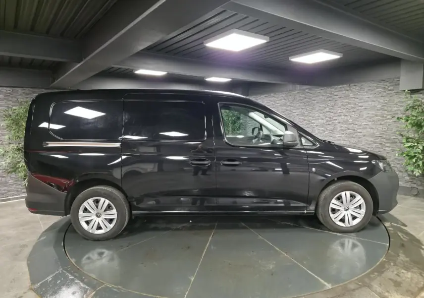 Vue latérale droite d'un Volkswagen Caddy Cargo noir 2024 avec jantes acier et porte coulissante tôlée.