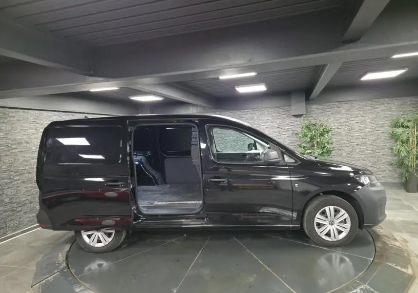 Vue latérale droite d'un Volkswagen Caddy Cargo noir 2024 avec porte coulissante ouverte en intérieur.