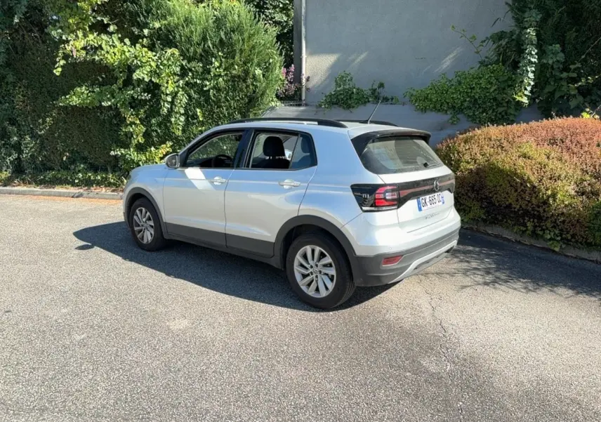 Volkswagen T-Cross gris clair vue 3/4 arrière droit, avec barres de toit noires et jantes alliage.
