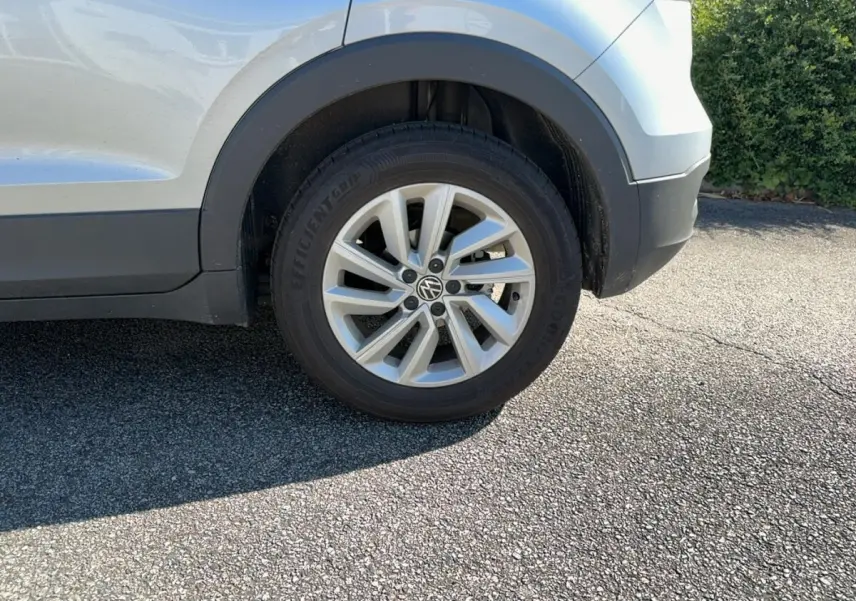 Gros plan sur la roue avant droite d’un Volkswagen T-Cross gris clair avec jante alliage et logo VW visible.