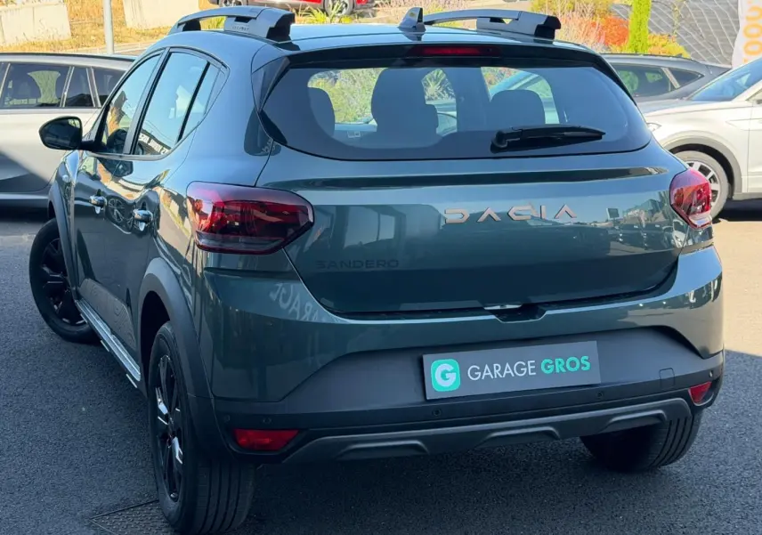 Vue 3/4 arrière droite d'une Dacia Sandero Stepway 2025 vert cèdre métallisé avec barres de toit et jantes noires.