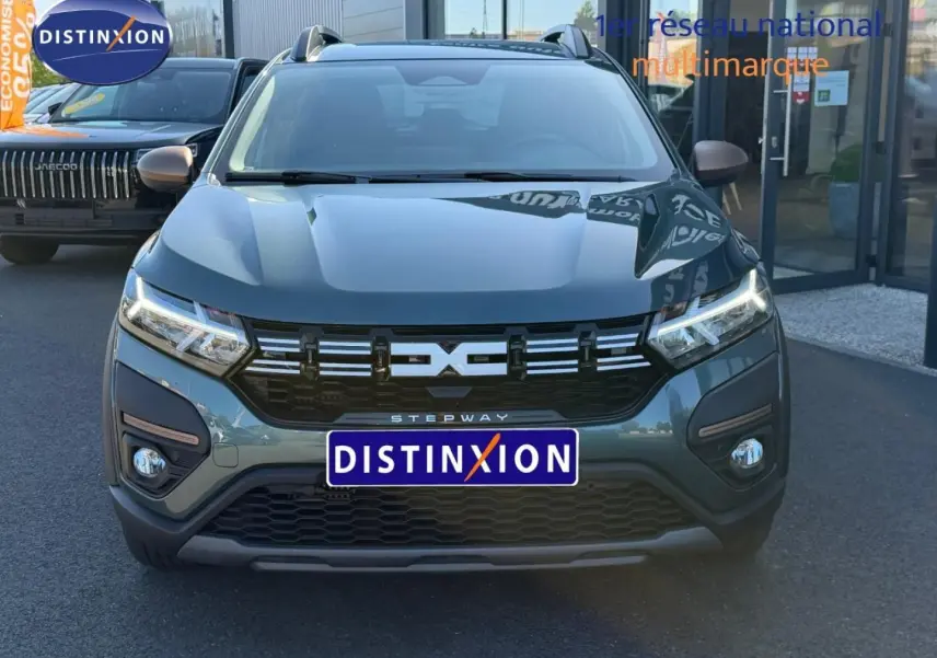 Vue avant d'une Dacia Sandero Stepway 2025 vert cèdre métallisé avec calandre noire et feux LED allumés.