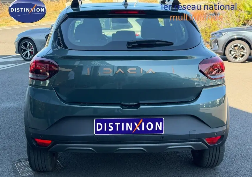 Vue arrière d'une Dacia Sandero 2025 vert cèdre métallisé avec logo DACIA et feux arrière LED visibles.