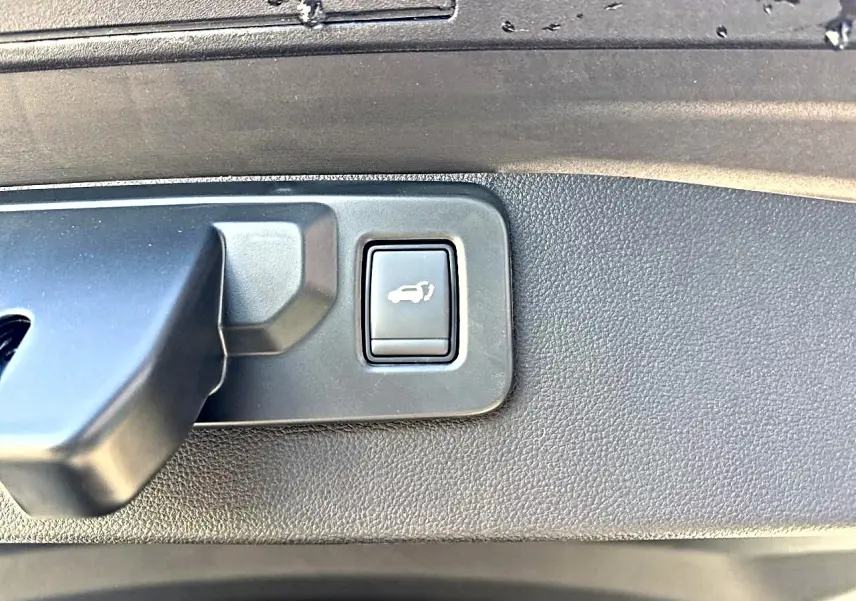 Gros plan sur le bouton d'ouverture électrique du hayon dans le coffre d'une Renault Symbioz gris rafale.
