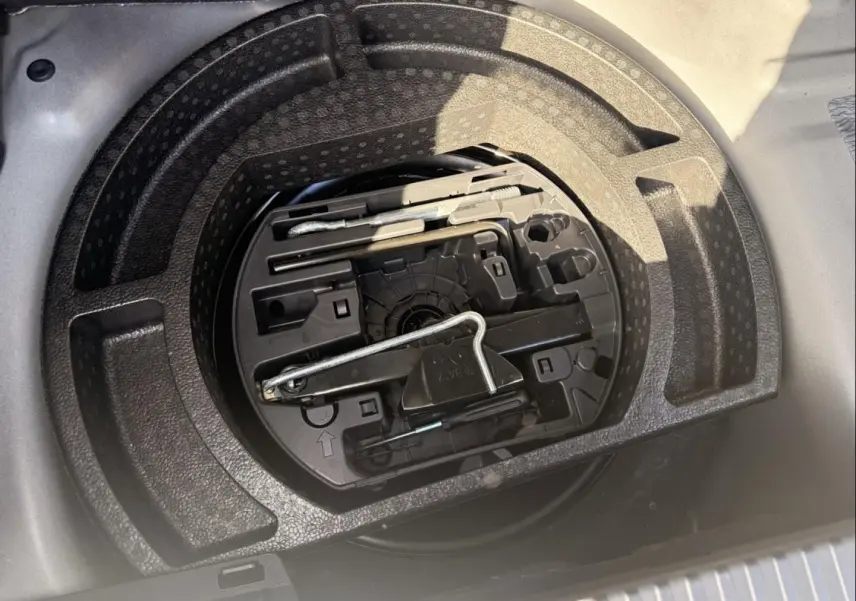 Vue plongeante sur le rangement sous coffre d'un Citroën C3 Aircross gris métal 2021, avec outils de dépannage visibles.