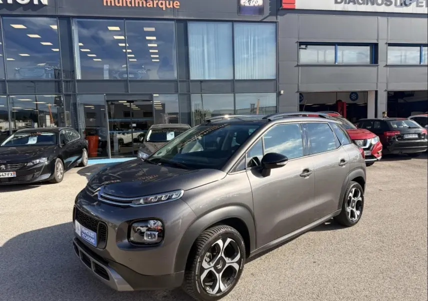 Citroën C3 Aircross gris métal en 3/4 avant droit, avec jantes distinctives et barres de toit visibles.