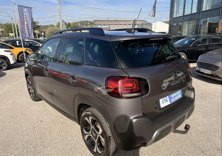 Citroën C3 Aircross gris métal vue 3/4 arrière droit, avec barres de toit et attelage visible.