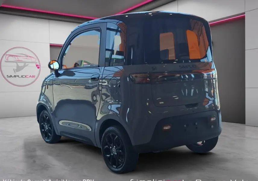 Vue 3/4 arrière droite de la SIMPLICI S1 électrique 2025 gris perle avec toit noir et jantes noires en intérieur showroom.