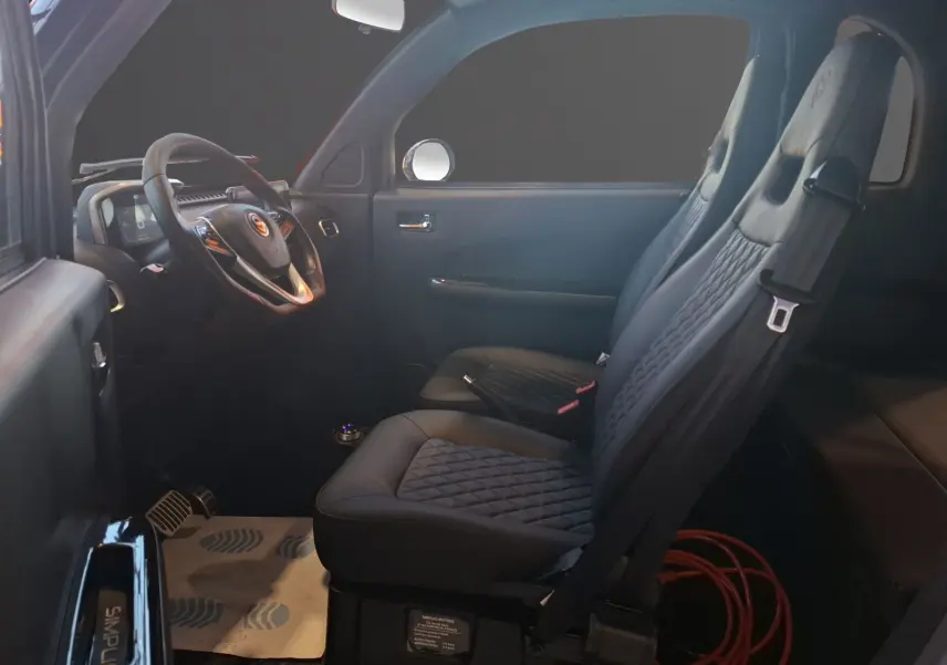 Vue intérieure côté conducteur de la SIMPLICI S1 2025 avec sièges noirs matelassés et volant multifonction.