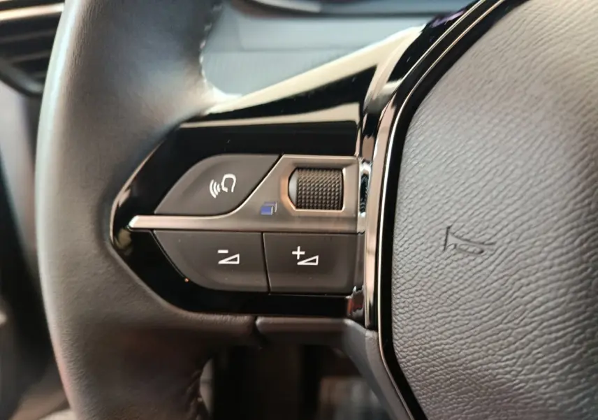 Gros plan sur les commandes du volant côté gauche en cuir noir de la Peugeot 208 PureTech 100 S&S Allure 2025.