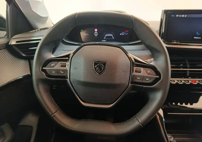 Vue rapprochée du volant cuir multifonctions et du tableau de bord numérique de la Peugeot 208 PureTech 100 S&S Allure 2025.