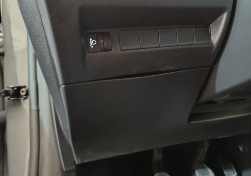 Détail du tableau de bord côté gauche en plastique noir avec commande de réglage des phares sur Peugeot 208 gris foncé.