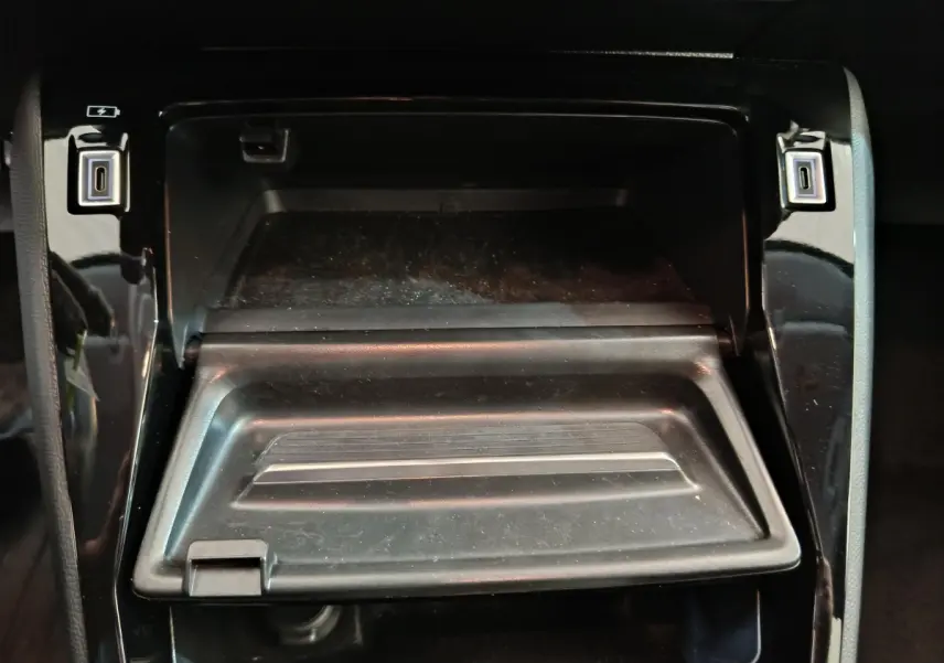 Vue rapprochée du rangement central ouvert avec ports USB dans l’habitacle noir brillant de la Peugeot 208 2025 gris foncé.