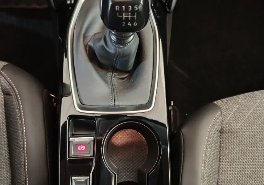 Vue plongeante sur la console centrale noire de la Peugeot 208 gris foncé avec levier de vitesse manuel et porte-gobelets.