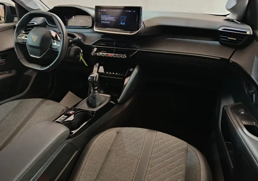 Intérieur avant droit de la Peugeot 208 gris foncé, volant cuir, écran tactile central et levier de vitesse manuel visibles.