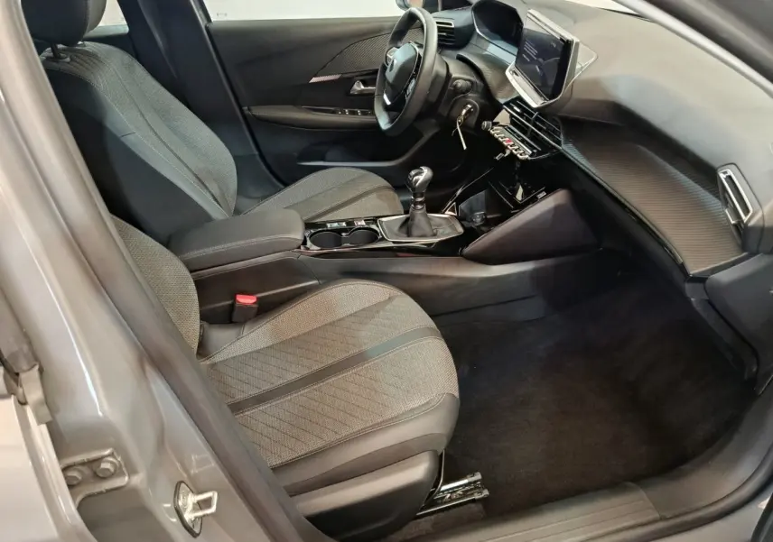 Intérieur avant droit de la Peugeot 208 gris foncé 2025, avec tableau de bord moderne et boîte manuelle.