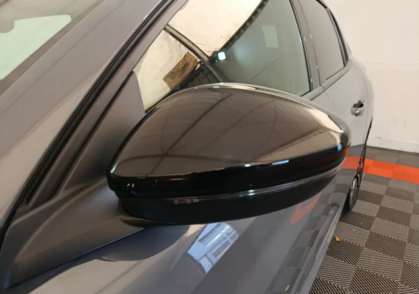 Rétroviseur noir côté gauche sur Peugeot 208 gris foncé, vue rapprochée du profil avant du véhicule.