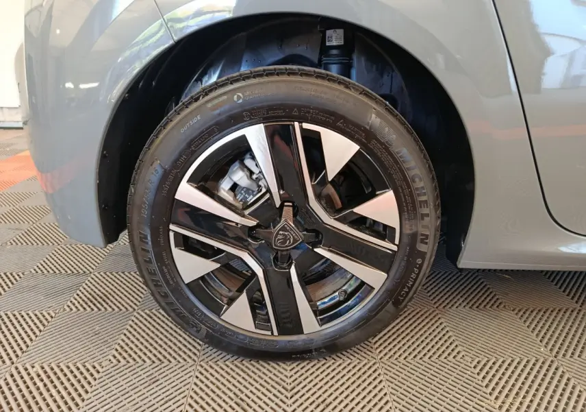 Gros plan sur la roue avant gauche grise d'une Peugeot 208 2025 avec jante alliage bicolore et logo lion central.