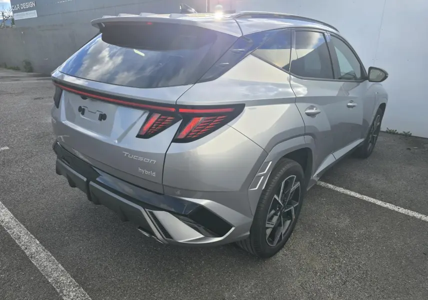 Vue 3/4 arrière droite du Hyundai Tucson 2025 hybride en argent métallisé avec feux arrière LED et jantes alliage noires.
